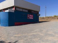 a sign on the side of a building by a desert road with a truck parked behind it