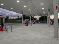 an empty gas station with many red pumps on the outside wall of it at dusk