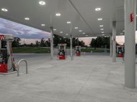 an empty gas station with many red pumps on the outside wall of it at dusk