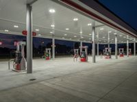 several gas pumps sit on concrete at a station with lights above them on an empty street