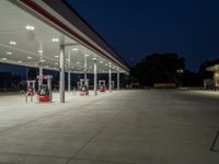 several gas pumps sit on concrete at a station with lights above them on an empty street