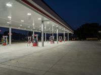 several gas pumps sit on concrete at a station with lights above them on an empty street