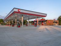 gas station at the edge of a street next to a large white building with red trimming