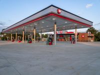 gas station at the edge of a street next to a large white building with red trimming