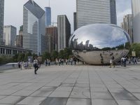 a crowd is gathering in a big public plaza near city buildings that have mirrored windows