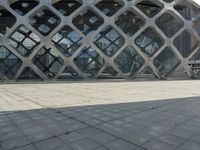 the concrete floor outside of an architectural building with geometric designs on it, along with a stone walkway and glass wall