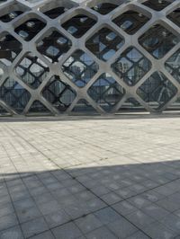 the concrete floor outside of an architectural building with geometric designs on it, along with a stone walkway and glass wall
