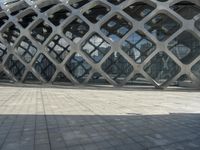 the concrete floor outside of an architectural building with geometric designs on it, along with a stone walkway and glass wall