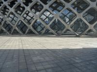 the concrete floor outside of an architectural building with geometric designs on it, along with a stone walkway and glass wall