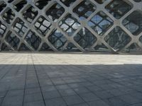 the concrete floor outside of an architectural building with geometric designs on it, along with a stone walkway and glass wall