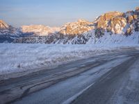 a person riding on the road in the middle of a snow covered landscape with mountains