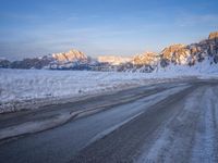 a person riding on the road in the middle of a snow covered landscape with mountains