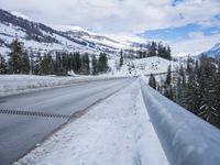 snow is covering the road between some trees and a mountain range below it that's covered in snow