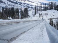 snow is covering the road between some trees and a mountain range below it that's covered in snow