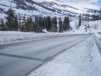snow is covering the road between some trees and a mountain range below it that's covered in snow