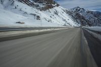a blurry shot of a snow covered mountain road, with snow covered mountains in the background