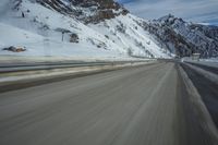a blurry shot of a snow covered mountain road, with snow covered mountains in the background
