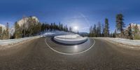 a 360 - ray lens image shows the road in snow - covered mountains and pine trees