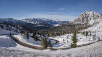 this is a wide wide snowy road in the mountains, which winds up and makes its way down to the mountain top