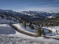 this is a wide wide snowy road in the mountains, which winds up and makes its way down to the mountain top