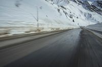 a speedboat travels on a wet road with snow and mountains in the background,