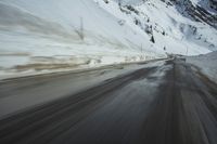 a speedboat travels on a wet road with snow and mountains in the background,
