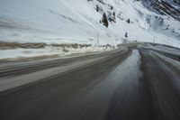 a speedboat travels on a wet road with snow and mountains in the background,