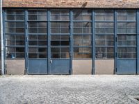 the empty brick walkway next to two blue garage doors and one in front has a dog laying on top of the floor