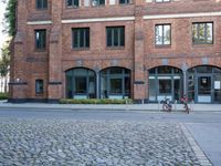 bicycles are parked on the sidewalk next to a brick building with three windows and one bike