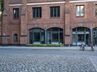 bicycles are parked on the sidewalk next to a brick building with three windows and one bike