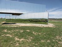 the reflection is seen on a mirrored wall and shows the surrounding green grass, rocks, and a couple of people