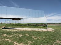 the reflection is seen on a mirrored wall and shows the surrounding green grass, rocks, and a couple of people