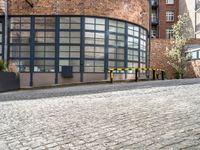 the back of an old red brick building is near many plants and trees in front of it