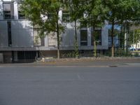 a large building with an entrance on a city street lined by tall green trees, and a small bench near it