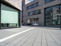 a building that has glass windows on it's front door and outside area of the building is covered in brick tiles and is grey