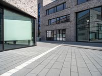 a building that has glass windows on it's front door and outside area of the building is covered in brick tiles and is grey