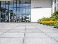 the sidewalk outside a white building with some windows, as well as plants and a flower garden