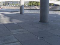 a couple of large pillars are sitting on the sidewalk near water and bridge to the right