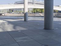 a couple of large pillars are sitting on the sidewalk near water and bridge to the right