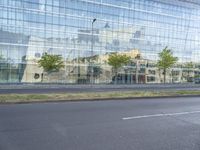 a glass building reflecting the building's architecture near a road side stop signal with trees