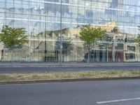 a glass building reflecting the building's architecture near a road side stop signal with trees