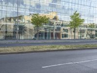 a glass building reflecting the building's architecture near a road side stop signal with trees