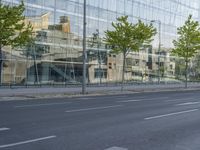 a glass building reflecting the building's architecture near a road side stop signal with trees