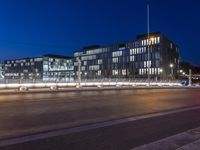 an intersection with several office buildings lit up at night, and a light trail across the street