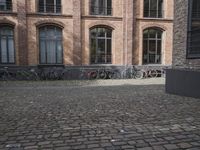 a row of bikes leaning up against a building wall in a courtyard area with brick flooring