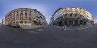 a 360 lens photo of two buildings in an intersection with cars and people passing each other on either side