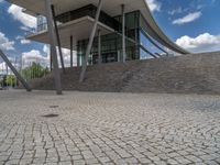 a person on a bike walking through a stone building entrance, in front of an enormous glass wall and stairs