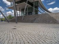 a person on a bike walking through a stone building entrance, in front of an enormous glass wall and stairs