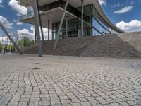 a person on a bike walking through a stone building entrance, in front of an enormous glass wall and stairs