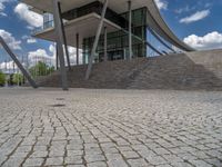 a person on a bike walking through a stone building entrance, in front of an enormous glass wall and stairs